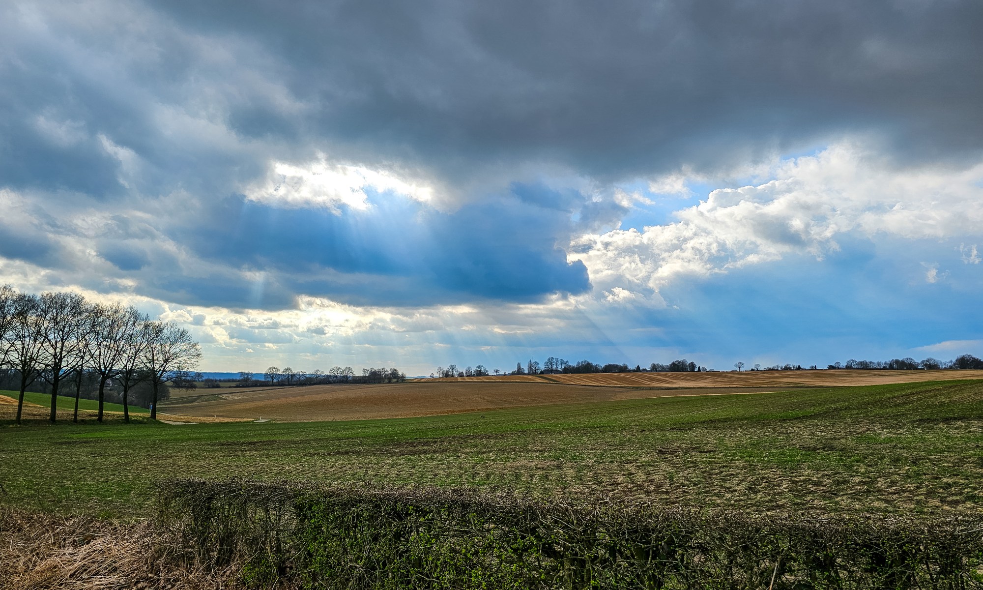 Sun is shining through two Openings in the Clouds on the fallow Fields in this layered Landscape